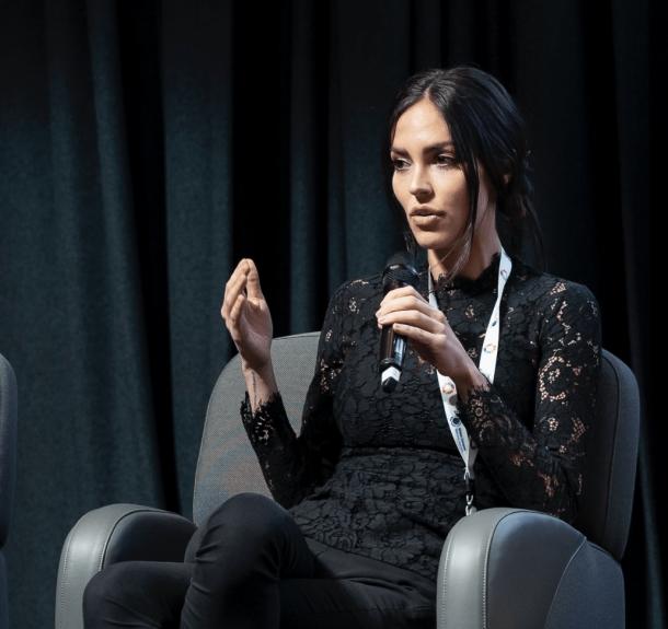 Natalie Kyriacou takes the floor at an event Picture of Natalie Kyriacou speaking at an event, sitting on a chair and holding a microphone
